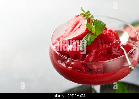 Granita di fragole o sorbetto di frutti di bosco fresco in vetro su sfondo grigio antico. Consistenza di gelato o sorbetto. Gelato con fragole e menta. Allora Foto Stock