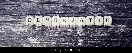 La parola tedesca per la democrazia posata da cubi di legno con lettere su fondo di legno Foto Stock