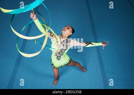 Danza, ginnastica ritmica e donna in palestra con nastro in aria, azione con vista dall'alto delle prestazioni e fitness. Atleta, atleta e ginnasta femminile Foto Stock