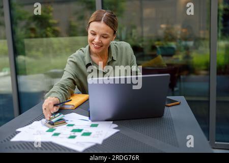 Donna manager che lavora con documenti e usa un computer portatile seduto sulla terrazza del bar Foto Stock