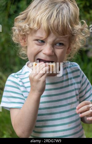 Un bambino morde in una pasta Foto Stock