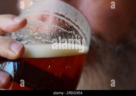 Un uomo che beve birra. Un uomo con la barba che beve una tazza di birra al pub Foto Stock