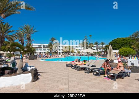 Tipica vista degli ospiti che si prendono il sole intorno ad una piscina in un hotel resort sull'isola di Lanzarote, Isole Canarie, Spagna Foto Stock