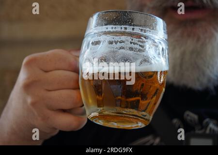 Un uomo che beve birra. Un uomo con la barba che beve una tazza di birra al pub Foto Stock