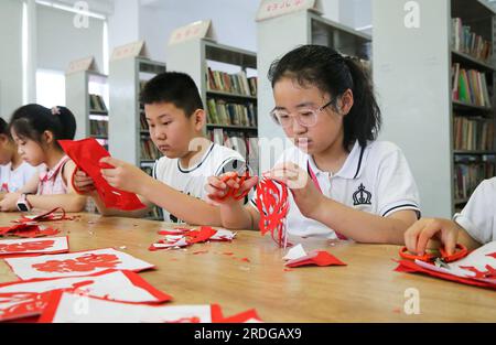 (230721) -- PECHINO, 21 luglio 2023 (Xinhua) -- i bambini imparano a fare opere d'arte per il taglio della carta nel distretto di Lianyungang City, provincia di Jiangsu della Cina orientale, 21 luglio 2023. (Foto di Wang Jianmin/Xinhua) Foto Stock