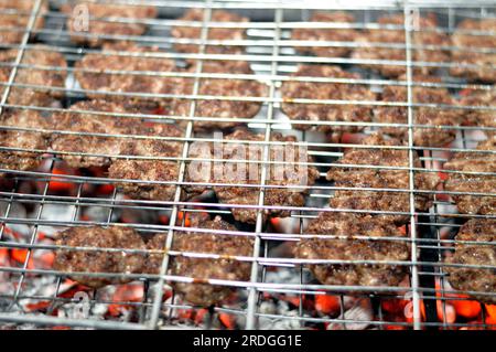 Polpette alla griglia kofta kufta di carne macinata di manzo in una rete a rete grigliata con manico su un carbone con fuoco e fuoco alla griglia, barbecue succoso Foto Stock