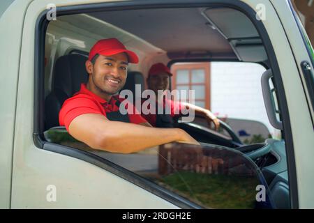 Il lavoratore del trasporto siede nel camion di carico, sorridendo con prontezza e dedizione mentre si imbarca per il trasferimento in una nuova casa. Il loro entusiasmo e impegno Foto Stock