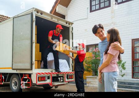 Una coppia asiatica sta insieme, osservando con anticipazione mentre i lavoratori si trasferiscono nella loro nuova casa. L'eccitazione riempie l'aria mentre si aspettano con ansia Foto Stock
