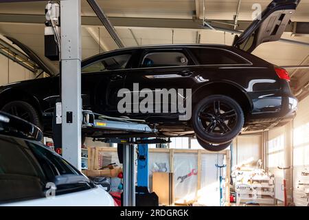 Centro di assistenza auto. Parte inferiore dietro il veicolo pov sollevato sul tecnico di sollevamento, eseguire la diagnosi e l'ispezione presso la stazione di manutenzione . Automobile Foto Stock