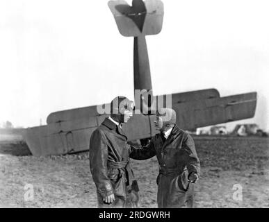 Hollywood, California: c. 1917 due piloti discutono il loro biplano che è naso giù sullo sfondo Foto Stock