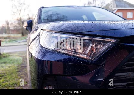 Un ritratto ravvicinato del faro sinistro di un'auto ibrida toyota rav4 blu scuro parcheggiata su un vialetto. Il veicolo può guidare elettricamente e su fossili Foto Stock