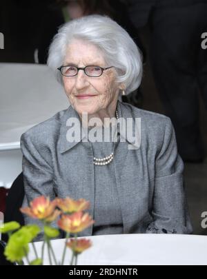 Senior femminile si siede a tavola restaurant. Ella è elegante e indossa una tuta grigia con perle. Lei è seduta serenamente in attesa per il suo cibo. Foto Stock