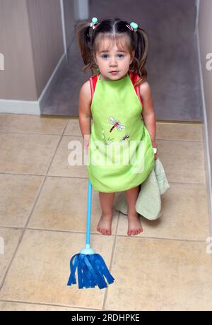 Tutte le mani sul ponte! Questa bambina è pronta e disposta ad aiutare sua madre con le faccende domestiche. Indossa il suo grembiule, tenendo il suo straccio spolverato Foto Stock