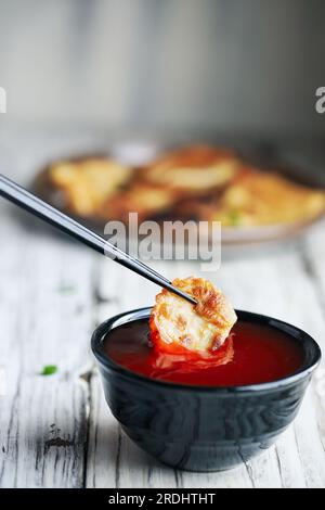 Bacchette che immergono un gnocco cinese fritto dorato, noto anche come Pot Sticker, in una ciotola di salsa rossa dolce e acida. Messa a fuoco selettiva con sfocatura Foto Stock