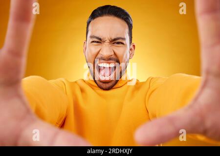 Grida, ritratto e selfie di un uomo arrabbiato in studio isolato su uno sfondo giallo. Faccia, urla e persona asiatica che scatta foto del profilo per Foto Stock