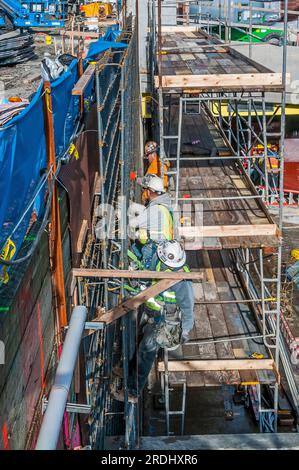 Gli operai edili con elmetti stanno lavorando su un armatura per un muro in un cantiere. Foto Stock