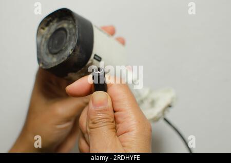 Dettaglio delle mani di un professionista esperto che lavora su una telecamera di sicurezza bianca, garantendo protezione e sorveglianza. Foto Stock