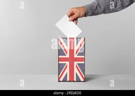 Uomo che mette il suo voto nelle urne decorate con la bandiera del Regno Unito su sfondo chiaro, primo piano Foto Stock