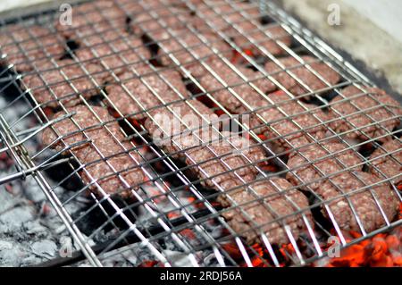 Polpette alla griglia kofta kufta di carne macinata di manzo in una rete a rete grigliata con manico su un carbone con fuoco e fuoco alla griglia, barbecue succoso Foto Stock