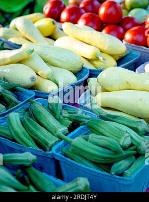 Sfondo alimentare di okra fresca, zucca gialla a collo di cocco e pomodori esposti in un mercato di prodotti. Foto Stock