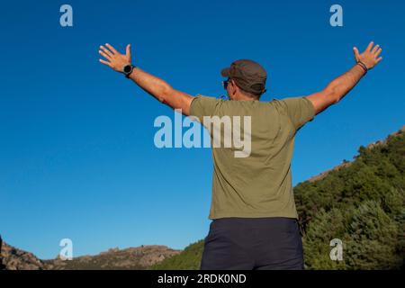 Uomo vestito con t-shirt verde militare, berretto e occhiali da sole che si gode una giornata in montagna Foto Stock