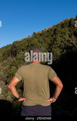 Uomo vestito con t-shirt verde militare, berretto e occhiali da sole che si gode una giornata in montagna Foto Stock