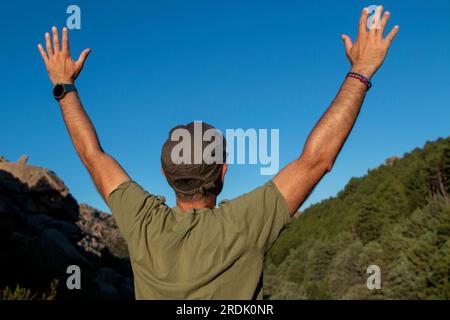 Uomo vestito con t-shirt verde militare, berretto e occhiali da sole che si gode una giornata in montagna Foto Stock