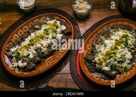 Enfrijoladas servito in un piatto di argilla. Tipico cibo messicano. Tacos di fagioli con crema e formaggio. Foto Stock