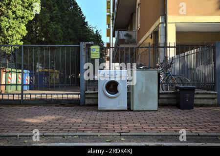 Lavatrice rotta e frigorifero sul marciapiede di una strada in una zona residenziale al tramonto Foto Stock