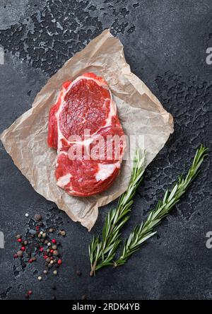 Filetto di bistecca cruda con pepe, sale e rosmarino sullo sfondo scuro del tavolo da cucina. Foto Stock
