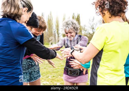Donne multigenerazionali felici che si accatastano le mani insieme prima dell'allenamento all'aperto - amici femminili che si divertono insieme all'aperto al parco cittadino - luminoso Foto Stock