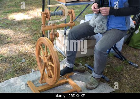 La donna filtra la lana grezza in filo con una ruota in legno che gira in un mercato di artigianato all'aperto, spazio per le copie, attenzione selezionata sulla mano Foto Stock