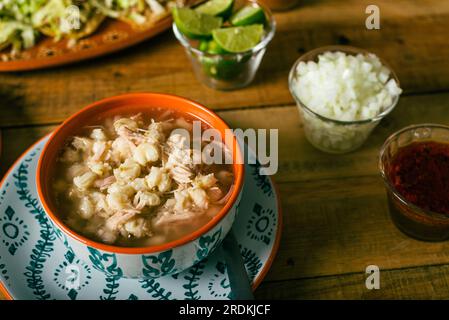 Pozole servito in un piatto profondo, con salsa e verdure su un tavolo di legno. Tipico cibo messicano. Foto Stock