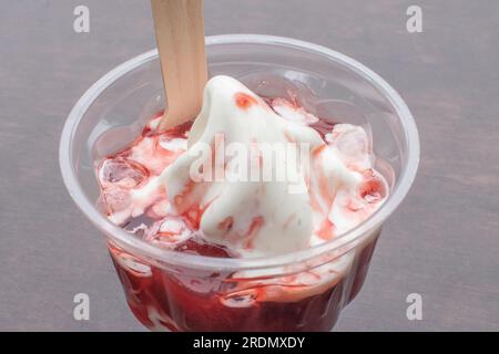 Un delizioso gelato servito in una tazza di plastica, condita con succulento sciroppo di frutta e riempita con appetitoso gelato alla fragola. Selettivo f Foto Stock