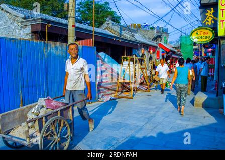 Pechino, CINA - quartieri della città vecchia cinese scena di strada - Hutong, operaio edile migrante che cammina lungo la strada con Wheelbarrel su Yandai Xiejie St., distretto di Xicheng, area dei laghi di Houhai, lavori di ristrutturazione Foto Stock