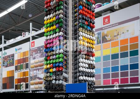 Interno del negozio di verniciatura. Rack con contenitori di vernice spray multicolore sullo sfondo di campioni di vernici venduti in negozio. Minsk, Bielorussia, 2023 Foto Stock