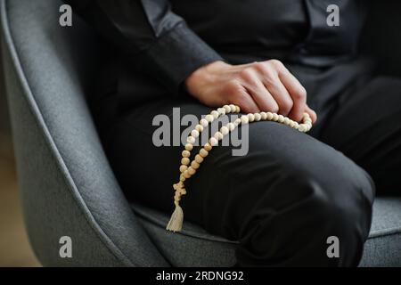 Primo piano di un uomo irriconoscibile che tiene il rosario sul grembo durante la sessione di terapia, copia spazio Foto Stock