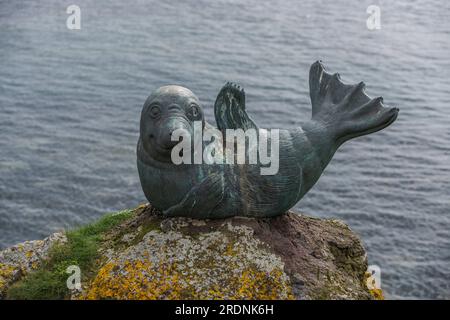 Statua in bronzo di una foca sorridente che sventola in posa umoristica su una roccia ricoperta di licheni nel porto di North Berwick, con un mare sfocato sullo sfondo Foto Stock