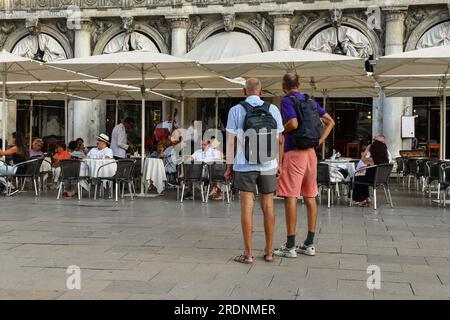 Due backpackers da dietro di fronte alla storica e lussuosa caffetteria del caffè Florian in Piazza San Marco in estate, Venezia, Veneto, Italia Foto Stock