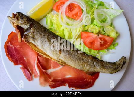 Piatto principale nel ristorante Asturiano, pesce trota intero alla griglia dal fiume di montagna servito con insalata mista fresca e pancetta Foto Stock