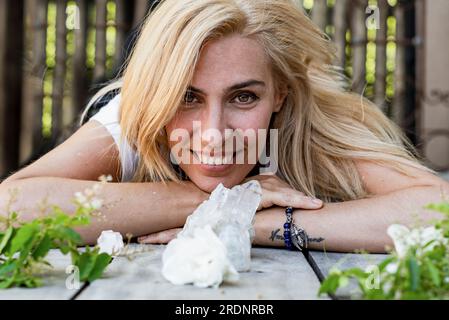 Ritratto di una bella donna sdraiata sul pavimento mentre guarda la fotocamera. Cristalli di quarzo bianco e rose intorno. Foto Stock