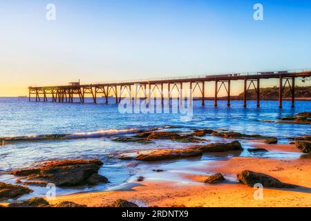 Lungo e storico molo presso la spiaggia Middle Camp di Catherine Hill Bay, cittadina costiera australiana, dalla spiaggia di sabbia con bassa marea. Foto Stock