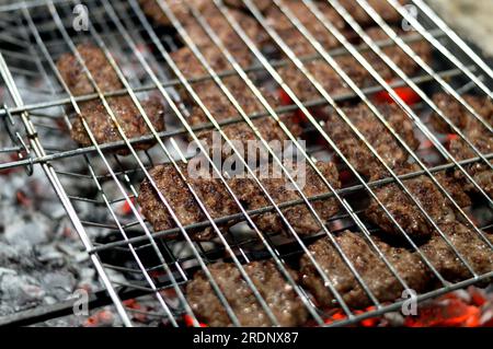 Polpette alla griglia kofta kufta di carne macinata di manzo in una rete a rete grigliata con manico su un carbone con fuoco e fuoco alla griglia, barbecue succoso Foto Stock