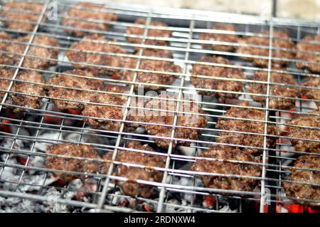 Polpette alla griglia kofta kufta di carne macinata di manzo in una rete a rete grigliata con manico su un carbone con fuoco e fuoco alla griglia, barbecue succoso Foto Stock