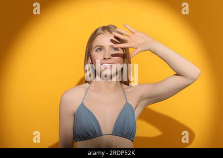 Bella giovane donna che si ombreggiava con la mano dalla luce del sole su sfondo arancione Foto Stock