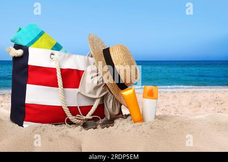 Borsa con zona bikini e accessori sulla soleggiata spiaggia dell'oceano, spazio per messaggi. Vacanze estive Foto Stock