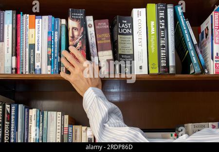 Mano che si avvicina per un libro sullo scaffale della biblioteca Foto Stock