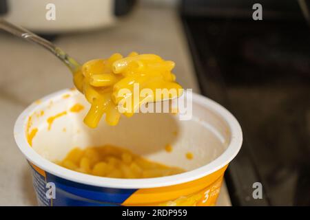 Cucchiaio di maccheroni e formaggio in una ciotola bianca e sullo sfondo della cucina Foto Stock