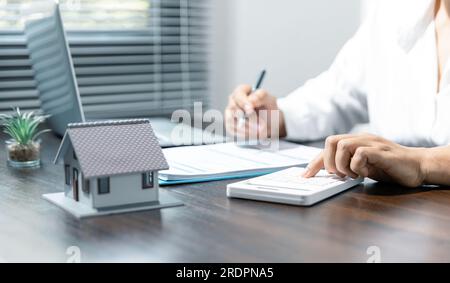 Avvicinare le mani femminili utilizzando la calcolatrice e scrivendo con i calcoli sulle spese dell'ufficio domestico. Foto Stock