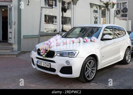 Bella macchina per matrimoni in una strada. Davanti all'auto di lusso decorata con fiori e fedi nuziali Foto Stock